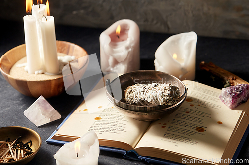 Image of magic book, sage, burning candles and ritual staff