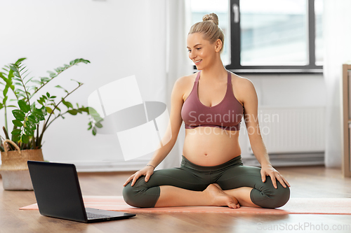 Image of pregnant woman with laptop doing yoga at home