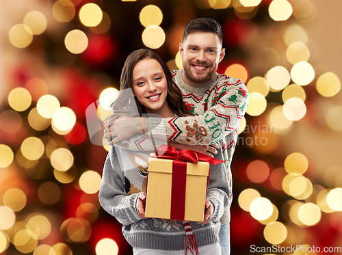 Image of happy couple in christmas sweaters with gift box