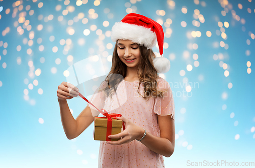 Image of teenage girl in santa hat opening christmas gift