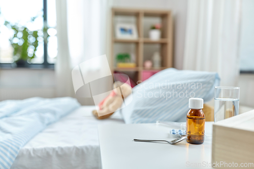 Image of medicine on table and teddy bear in bed at home