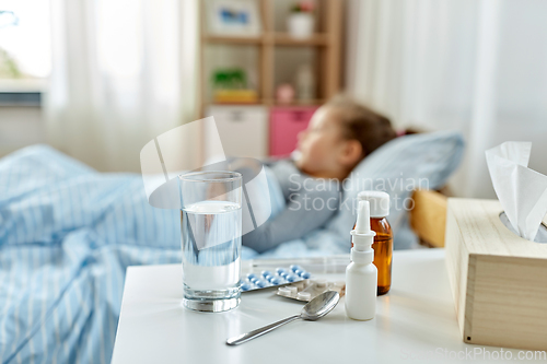 Image of medicine for sick little girl lying in bed at home