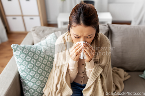 Image of sick woman blowing nose in paper tissue at home