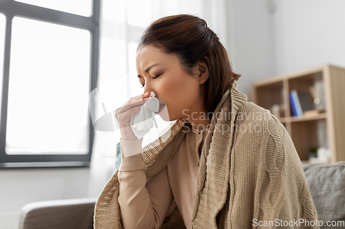 Image of sick woman blowing nose in paper tissue at home