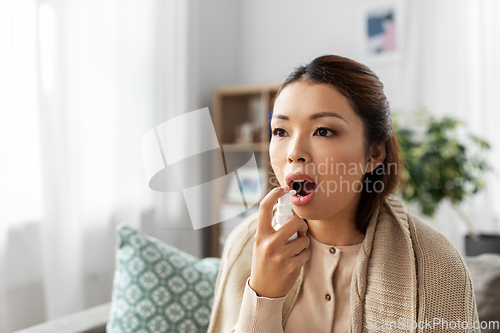 Image of sick asian woman using oral spray medicine at home