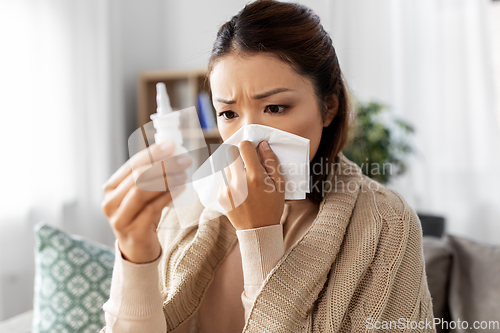 Image of sick asian woman with nasal spray blowing nose