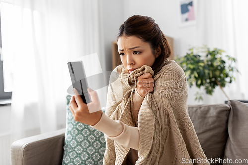 Image of sad sick woman in blanket using smartphone at home