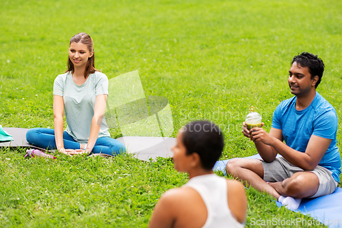 Image of group of people sitting on yoga mats at park