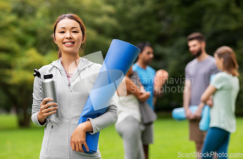 Image of smiling woman with yoga mat and bottle at park