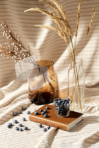 Image of cup of blueberry, book and dried flowers in vases