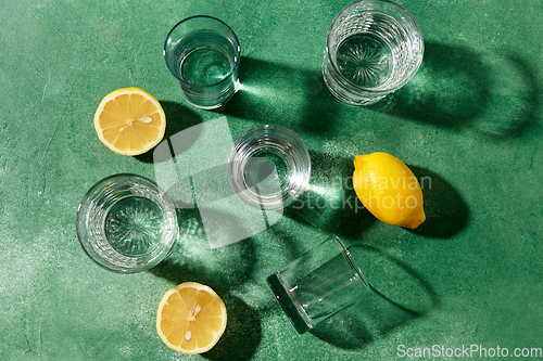 Image of glasses with water and lemons on green background