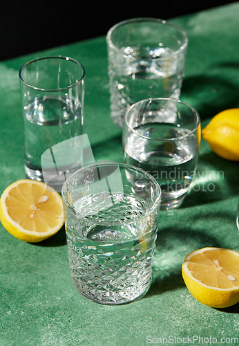 Image of glasses with water and lemons on green background