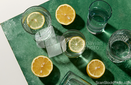 Image of glasses with water and lemons on green background