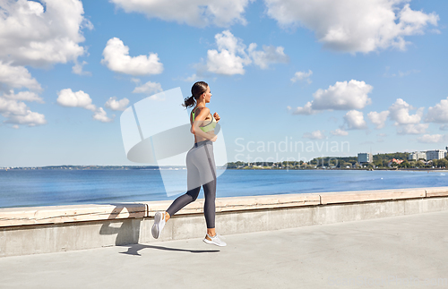 Image of young woman running along sea promenade