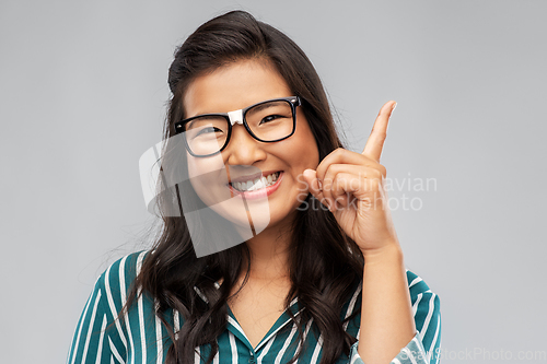 Image of happy asian woman in glasses pointing finger up