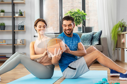Image of happy couple exercising with ball at home