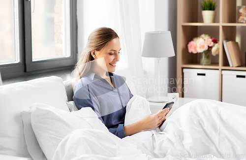 Image of young woman with smartphone in bed in morning