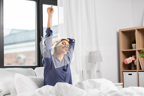 Image of happy woman stretching in bed at home