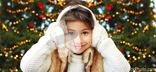 Image of happy little girl in earmuffs over christmas trees