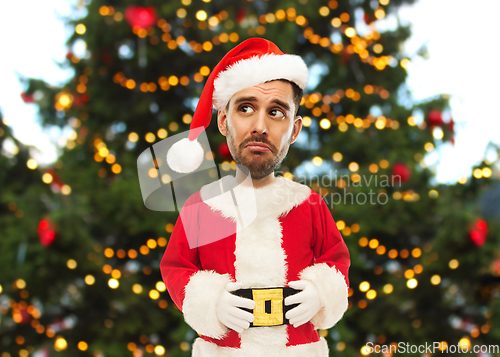 Image of sad man in santa claus costume over christmas tree