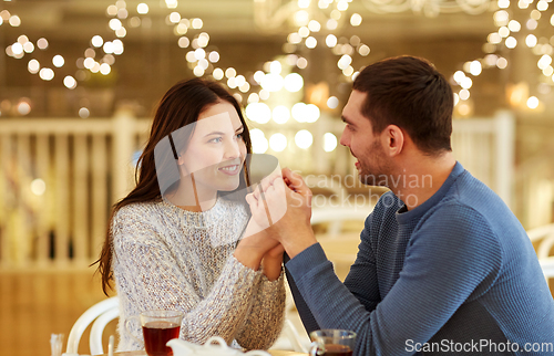 Image of happy couple with tea holding hands at restaurant
