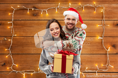 Image of happy couple in christmas sweaters with gift box