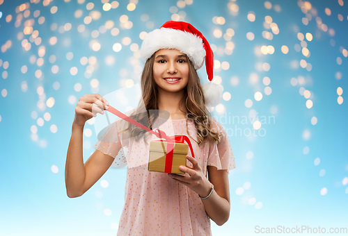 Image of teenage girl in santa hat opening christmas gift