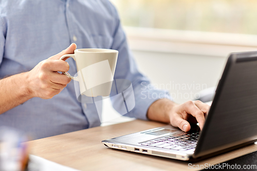 Image of man with laptop drinking coffee at home office