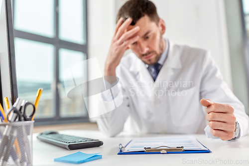 Image of stressed male doctor with clipboard at hospital