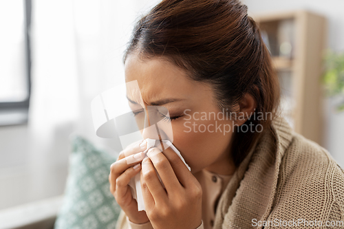 Image of sick woman blowing nose in paper tissue at home