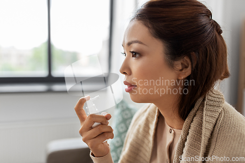 Image of sick asian woman using oral spray medicine at home