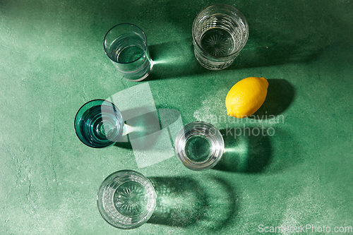 Image of glasses with water and lemons on green background