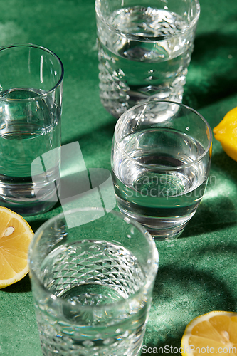 Image of glasses with water and lemons on green background