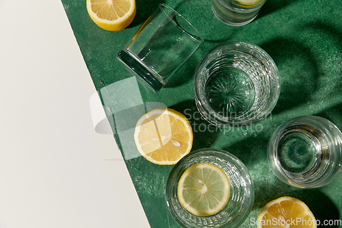 Image of glasses with water and lemons on green background