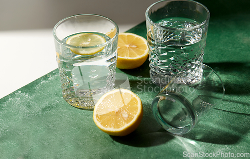 Image of glasses with water and lemons on green background