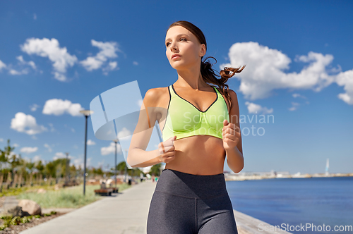 Image of young woman running along sea promenade