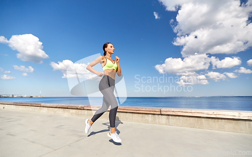 Image of young woman running along sea promenade