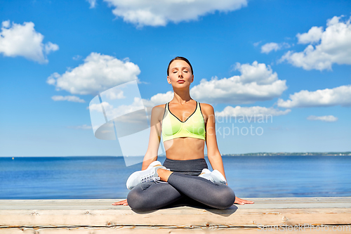 Image of young woman meditating in lotus pose at seaside