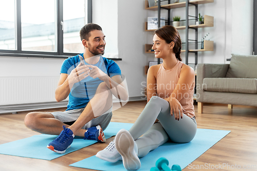 Image of happy couple with smartphone doing sports at home