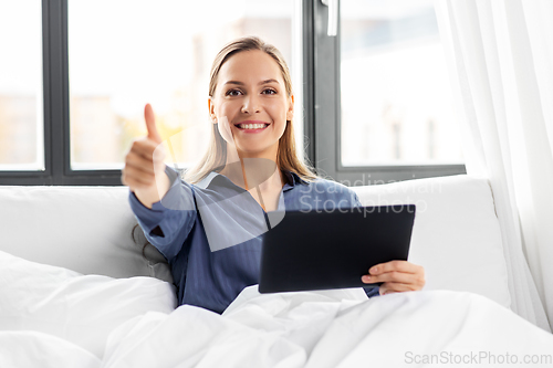 Image of woman with tablet pc in bed showing thumbs up