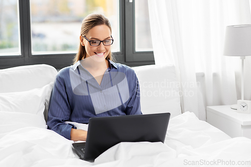 Image of young woman with laptop in bed at home bedroom