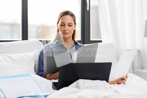 Image of young woman with laptop and papers in bed at home