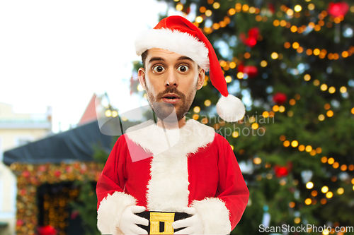 Image of surprised man in santa costume over christmas tree