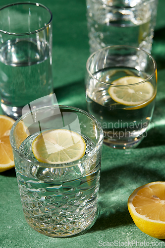 Image of glasses with water and lemons on green background