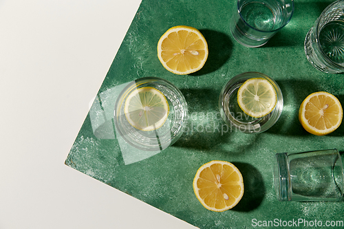 Image of glasses with water and lemons on green background