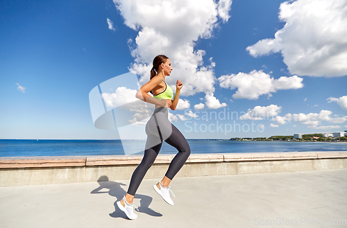 Image of young woman running along sea promenade