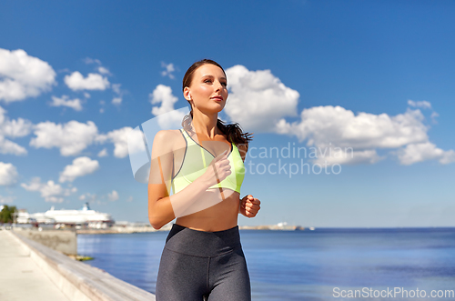 Image of woman with wireless earphones running at seaside