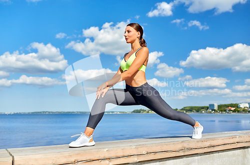 Image of happy young woman doing sports and stretching leg