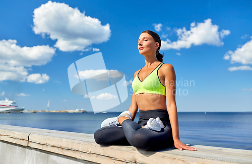 Image of young woman meditating in lotus pose at seaside