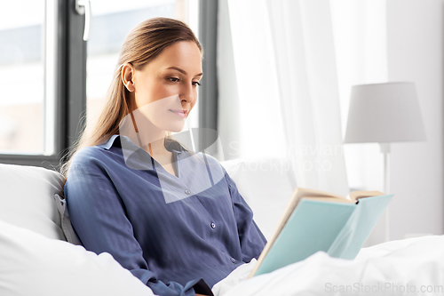 Image of young woman reading book in bed at home